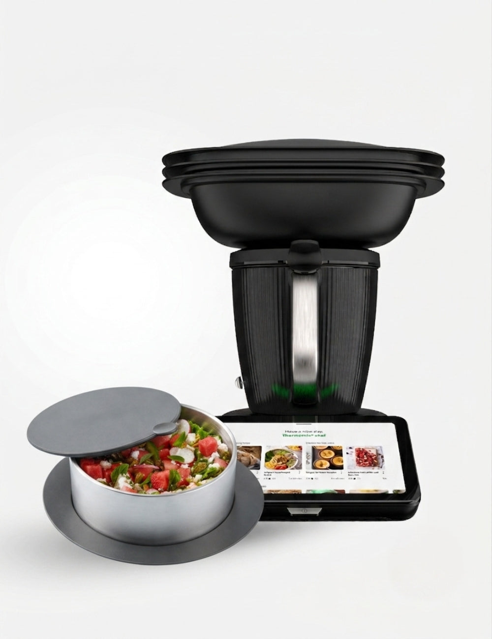 A black countertop kitchen appliance with a lid, shown alongside a stainless steel bowl filled with chopped vegetables and a tablet displaying a recipe screen, on a light gray background.